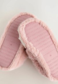 Roze faux-fur slippers met een gestructureerde rubberen zool, voorzien van een fluffy bovenkant en een reliëfmerknaam op de binnenzool.