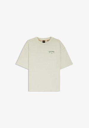 Jasnobeżowa koszulka z krótkim rękawem, okrągłym dekoltem i małym zielonym napisem "RIO DE JANEIRO" na górnej lewej części klatki piersiowej.