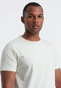 Camiseta de algodón blanca con mangas cortas, detalles de costura sutiles y un logo bordado "Ombre" en el pecho.