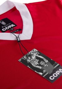 Rød sportsjersey med en hvid krave; indeholder et stofmærke med teksten "COPA" og et vedhæftet sort-hvidt billede af en trofæfejring.