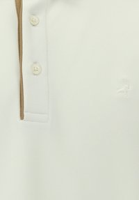 Weißes Poloshirt aus strukturiertem Stoff mit braunem Kragenbesatz, zwei Knopf-Leiste und einem kleinen bestickten Logo auf der Brust.