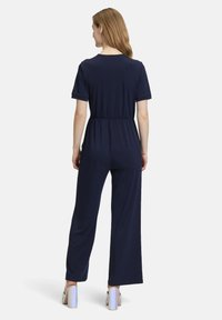 Marineblauwe jumpsuit van zachte stof met korte mouwen, elastische taille en wijde pijpen. Heeft een ronde halslijn en simpele stiksels.
