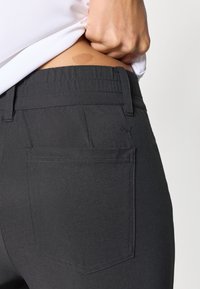 Σκούρο γκρι παντελόνι από λείο ύφασμα, με μία πίσω τσέπη που φέρει μικρό λογότυπο και ζώνη μέσης με διακριτικές λεπτομέρειες ραφών.