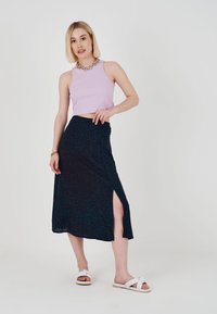 Ljuslila ribbad crop top i kombination med en mörkblå kjol med ett subtilt mönster och en sidoklyvning, kompletterad med vita sandaler.
