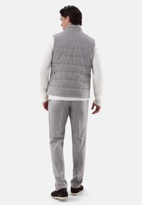 Graue Steppweste mit hohem Kragen, kombiniert mit einem strukturierten weißen Strickpullover und hellgrauen Hosen. Braune Schuhe vervollständigen den Look.