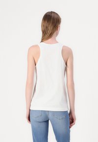 Witte tanktop van katoen, met een ontspannen pasvorm, brede banden en een ronde hals. G gedragen met lichtblauwe spijkerbroek, op een effen achtergrond.