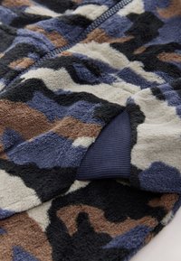 Tissu en polaire à motif camouflage avec des nuances de bleu, noir et marron, une surface texturée et une bordure côtelée bleu marine.