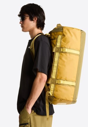 Mochila en amarillo y verde oliva, hecha de tela resistente. Cuenta con correas ajustables, hebillas y una forma cilíndrica estructurada.