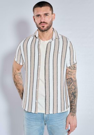 Kurzarmhemd mit vertikalen Streifen in Beige, Weiß und Schwarz. Durchgehende Knopfleiste, leichtes Material, mit einem schlichten weißen T-Shirt darunter.
