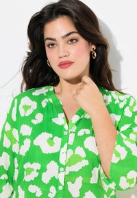 Grüne knöpfbare Bluse mit einem mutigen weißen und hellgrünen Tierdruck, einem V-Ausschnitt und luftigen Ärmeln.