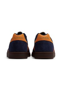 Marinblå mockasneakers med orange detaljer, runda tår, platt brun gummisul och präglad logotyp på baksidan.