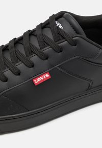 Fekete bőrsportcipő kerek orral, vastag fekete fűzőkkel és piros Levi's logóval az oldalán. Simább textúrával és gumitalppal tervezve.