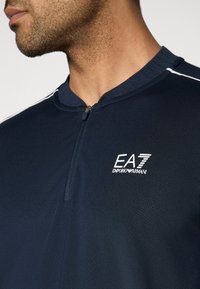 Μπλε ναυτικό αθλητικό πουκάμισο με φερμουάρ, με υφή, που διαθέτει ψηλό γιακά, λευκές ρίγες ως δ ιακοσμητικά στοιχεία και κεντημένο λογότυπο EA7 στο στήθος.
