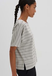 Lightweight, short-sleeve top in cream with black zigzag pattern, featuring a boxy shape and side slits for ease of movement.
