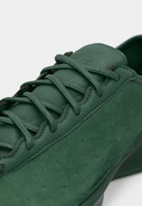 Πράσινα δερμάτινα παπούτσια με υφή στο φινίρισμα, διαθέτοντας κορδόνια στο ίδιο χρώμα και στρογγυλεμένο σχέδιο στη μύτη. Ραφές διακοσμητικές κατά μήκος των άκρων.