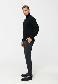 Fekete garbó pulóver hosszú ujjakkal, sötétszürke, testhez simuló nadrággal és fekete loaferekkel párosítva. Sima textúra, laza szabás.