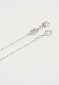 Zilveren ketting met een kreeftsluiting, een achthoekige logo-hanger en een gefacetteerde kristallen hanger. De schakels van de ketting zijn delicaat en glanzend.
