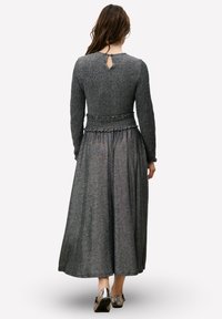 Robe longue grise en tissu texturé avec manches longues et taille cintrée. Elle présente un détail dos en forme de goutte d'eau et une jupe fluide.