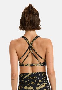 Reggiseno sportivo nero con spalline incrociate, caratterizzato da un motivo astratto verde. Il materiale sembra elastico, con una texture liscia e opaca.