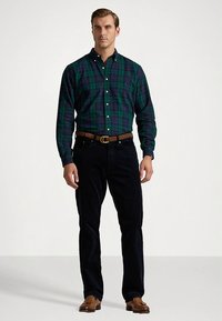 Πουκάμισο με πράσινο και μπλε καρώ, γιακά, κουμπιά και μακριά μανίκια, συνδυασμένο με σκούρο μπλε τζιν και καφέ ζώνη. Καφέ παπούτσια ολοκληρώνουν το ντύσιμο.