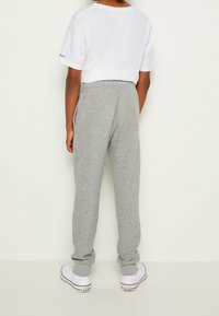 Grå sweatpants med elastiske manchetter, lavet af blødt stof. Sættes sammen med en hvid T-shirt med korte ærmer og hvide sneakers med røde accenter.