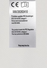 Vit tygetik som visar CE-märket, produktinformation och säkerhetsinstruktioner. Text på flera språk, inklusive "Håll borta från eld."