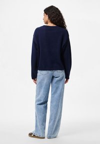 Suéter de malha oversized azul-marinho com decote redondo, combinado com calças de ganga largas azul-claro, apresentando uma ligeira flare na barra.