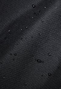 Tessuto impermeabile nero caratterizzato da una texture liscia con gocce d'acqua visibili sparse sulla superficie.