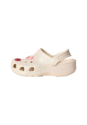 Sabot beige texturé avec des trous de ventilation, une bride arrière réglable, et des breloques décoratives en forme de fleurs roses et rouges sur le dessus.