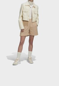 Kremowa, jeansowa kurtka krótka, beżowe bawełniane szorty, biała bluzka z długim rękawem, kremowe sneakersy z beżowymi akcentami, pasujące jasne skarpetki.