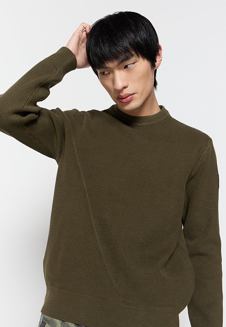 Maglione a coste verde oliva con collo alto, maniche aderenti, tessuto testurizzato e vestibilità rilassata. Presenta una sottile rifinitura delle cuciture.