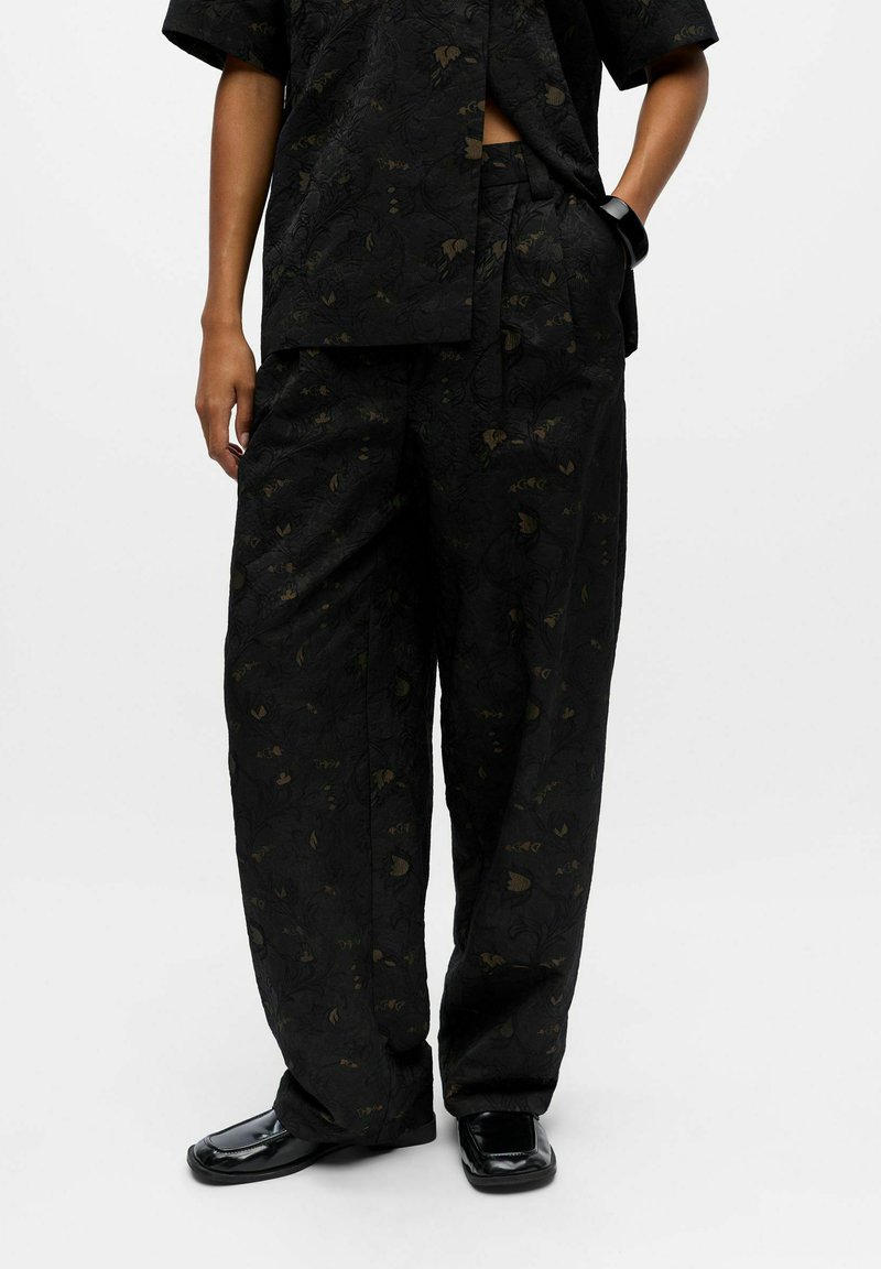 Schwarz gemustertes Outfit mit locker sitzenden, weit geschnittenen Hosen und einem passenden kurzärmeligen Oberteil, beide mit subtilen floralen Texturen und grünen Akzenten.