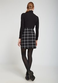 Top negro de manga larga, ajustado. Falda corta negra con un patrón de cuadros grises. Medias negras. Zapatos negros gruesos con suelas texturizadas.