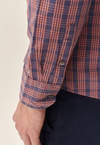 Button-up shirt featuring a navy and orange plaid pattern, cotton material, long sleeves, and buttoned cuffs with a smooth texture.