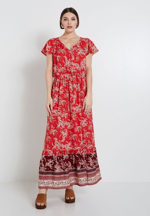 Vestido maxi rojo con patrón floral, escote en V y mangas acampanadas. Presenta una cintura ajustada y un dobladillo en capas con patrones contrastantes. Zapatos marrones.