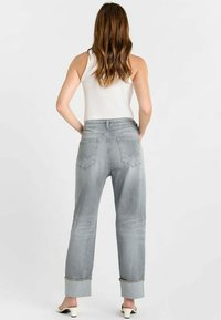 Lichtgrijze denim jeans met een losse pasvorm, opgerolde uiteinden en twee achterzakken. Gezien van achteren, gecombineerd met een wit tanktop.