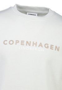 Sudadera gris claro con "COPENHAGUE" en texto beige y blanco. Presenta un cuello redondo y una textura suave. Etiqueta de la marca visible en el interior.