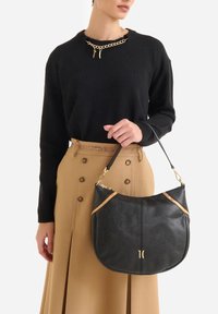 Borsa hobo in pelle nera con inserti marrone chiaro e ferrature dorate. Texture liscia, forma arrotondata e tracolla corta.