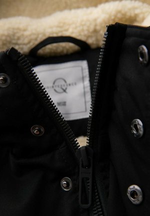 Veste noire à l'extérieur lisse avec une doublure en shearling beige. Dotée d'une fermeture éclair métallique et de boutons-pression, avec une étiquette d'entretien en tissu à l'intérieur.