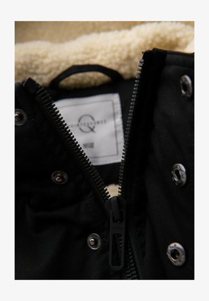 Veste noire à l'extérieur lisse avec une doublure en shearling beige. Dotée d'une fermeture éclair métallique et de boutons-pression, avec une étiquette d'entretien en tissu à l'intérieur.