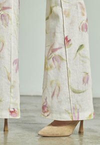 Beige suède pumps met spitse neuzen, gedragen bij witte broek met wijde pijpen met een zacht roze en groen bloemmotief.