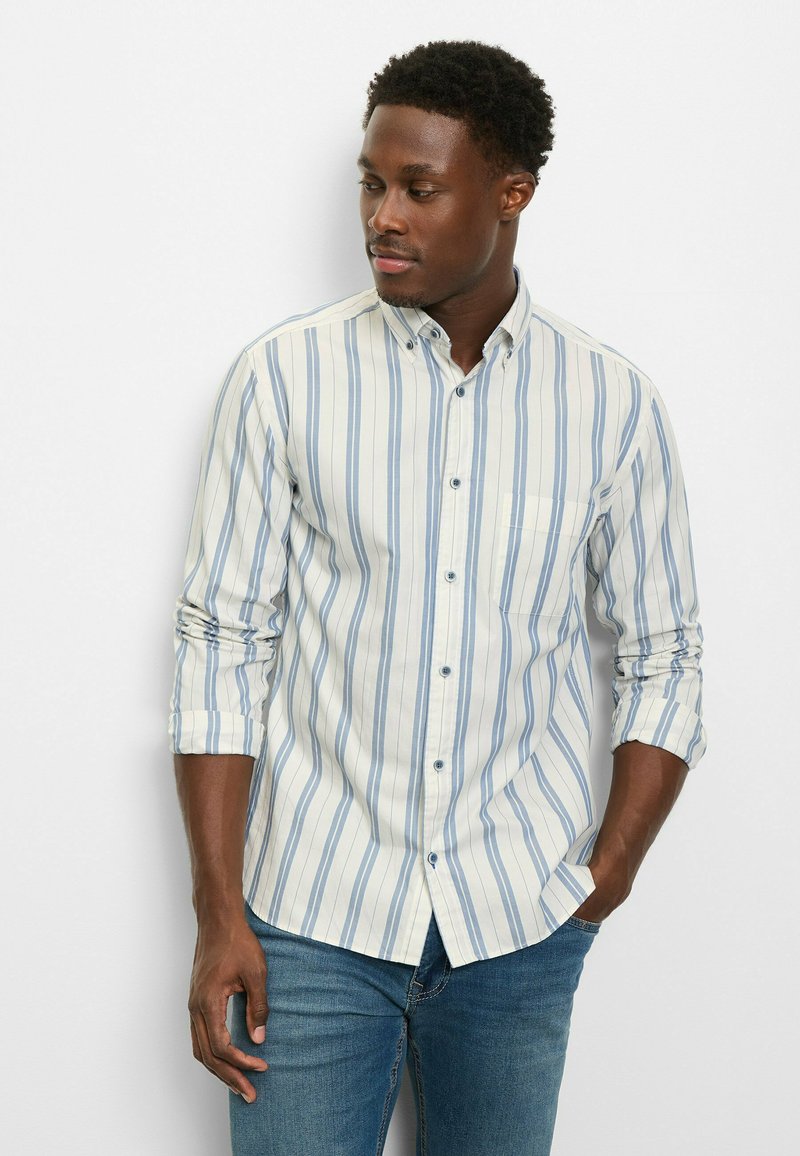 Hellblau-weiß gestreiftes Hemd aus Baumwolle mit Knöpfen, einer Tasche und aufgekrempelten Ärmeln, kombiniert mit Jeans.