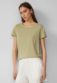 Olijfgroen katoenen t-shirt met korte mouwen en een ronde halslijn, gedragen met lichtgekleurde, gestructureerde shorts. Gladde stof, casual pasvorm.