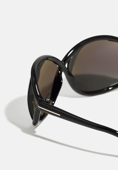 Occhiali da sole neri con montatura lucida e lenti marroni. Presentano un design elegante e un accento dorato sulle astine.