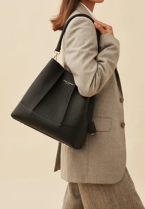 Zwarte leren tote bag met een gestructureerd ontwerp, voorzien van een klepdetail en gouden hardware. De tas heeft een gladde textuur en stevige handvat.