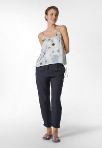 Top leggero e fluido con motivi ad acquerello blu; abbinato a pantaloni larghi in lino blu scuro e ciabatte blu.