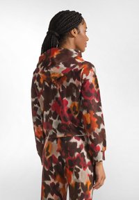 Felpa con cappuccio in tessuto morbido, caratterizzata da una stampa leopardata astratta nei colori arancione, rosso e marrone, con un design cropped e polsini a costine.