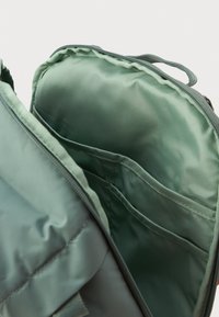 Interi�ér zelenej látkovej batohu s mäkkou textúrou, obsahujúci niekoľko priehradok a zipsové uzatváranie. Rukoväte v zhodnej farbe sú viditeľné.