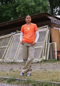 Orange Nike fotbollströja med en lejongrafik, som är kombinerad med ljusbeige byxor. Outfitten har ett texturerat mönster och en avslappnad design.