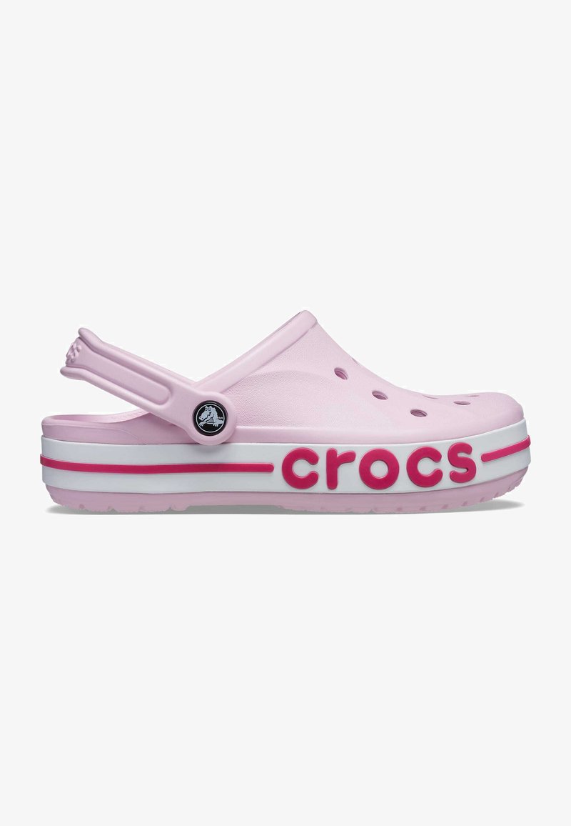 Clog Crocs rose clair avec des trous de ventilation, une sangle de talon ajustable, une semelle blanche avec des détails roses, et "crocs" embossé sur le côté.